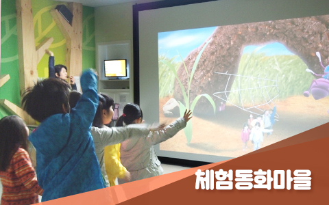 체험동화마을 사진. 어린이들이 스크린에 비치는 영상을 보며 손을 흔들고 있다.